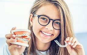 Girl holding false teeth with sample braces in one hand and Invisalign in the other