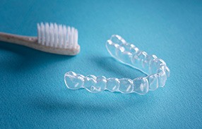 Clear aligner next to toothbrush on blue surface