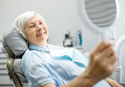 a dental implant patient checking her smile with a mirror