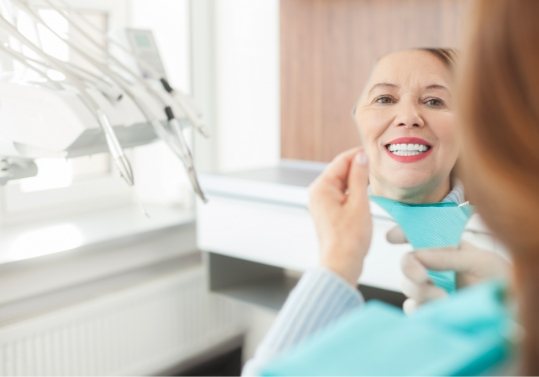 Woman in dental chair admiring her smile in mirror