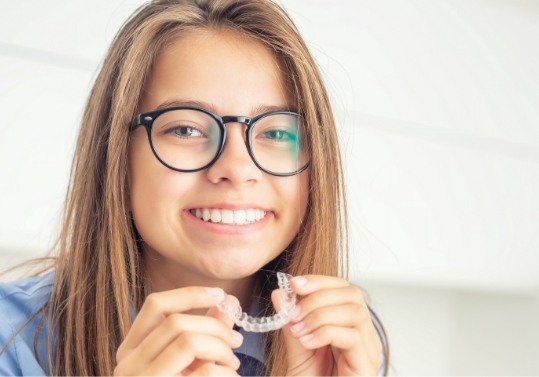 Smiling young woman holding Invisalign aligner for orthodontics in Fountain Valley
