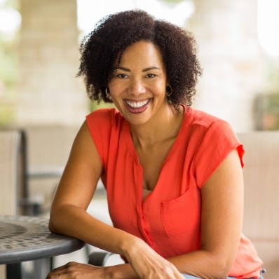 Woman in orange blouse smiling after restorative dentistry in Fountain Valley