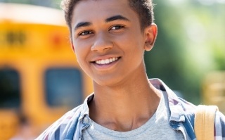 Teenage boy wearing backpack smiling with school bus in background