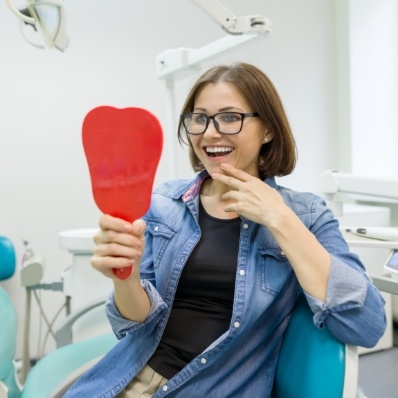 Young brunette woman in dental chair looking at her smile in red mirror