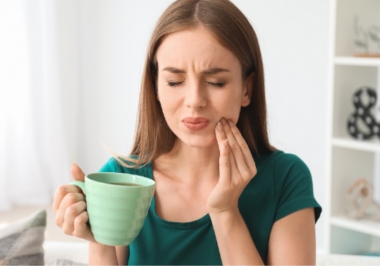 Young woman with green coffee mug holding her cheek in pain
