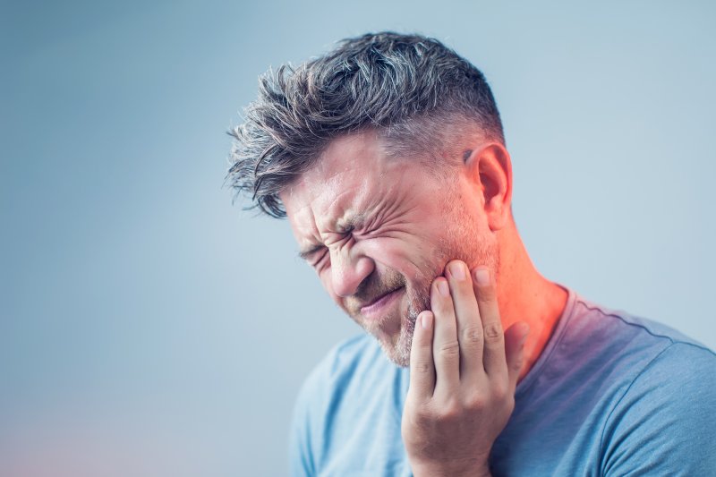 person experiencing tooth pain holding their cheek